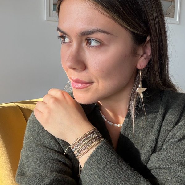 Model wearing stacked LeJu Glimmer bracelets with a grey knit