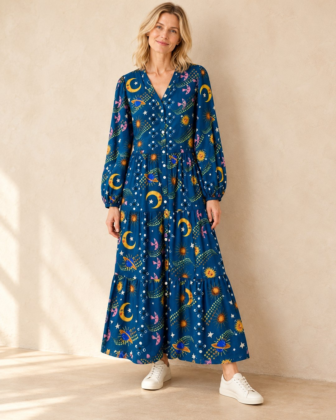 Model wearing the blue celestial print maxi dress with cream leather trainers on a beige background