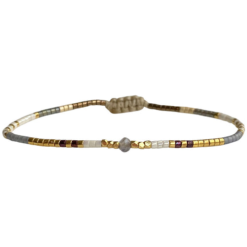 Handwoven in Colombia, this delicate bracelet features a single row of Japanese glass beads in gold and neutral tones with a Iolite, stone of the muses and creativity, in the centre.  Wear this stylish bracelet alone or as a part of a bracelet layering combination, with your favourite outfits.  Details:  - Japanese glass beads  - Gold vermeil faceted beads  - Iolite semi-precious stone  - Width: 2mm  -Can be worn in the wate