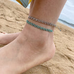 MACRAME ANKLET IN METALLIC GREEN TONES WITH SILVER BEADS ON MODEL